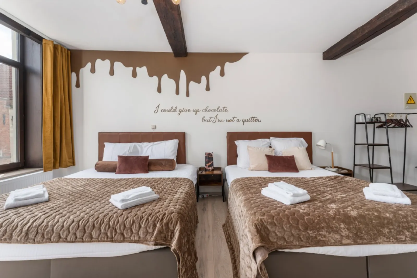 Two double beds side by side under dark timber beams, with a chocolate drip painted on the wall