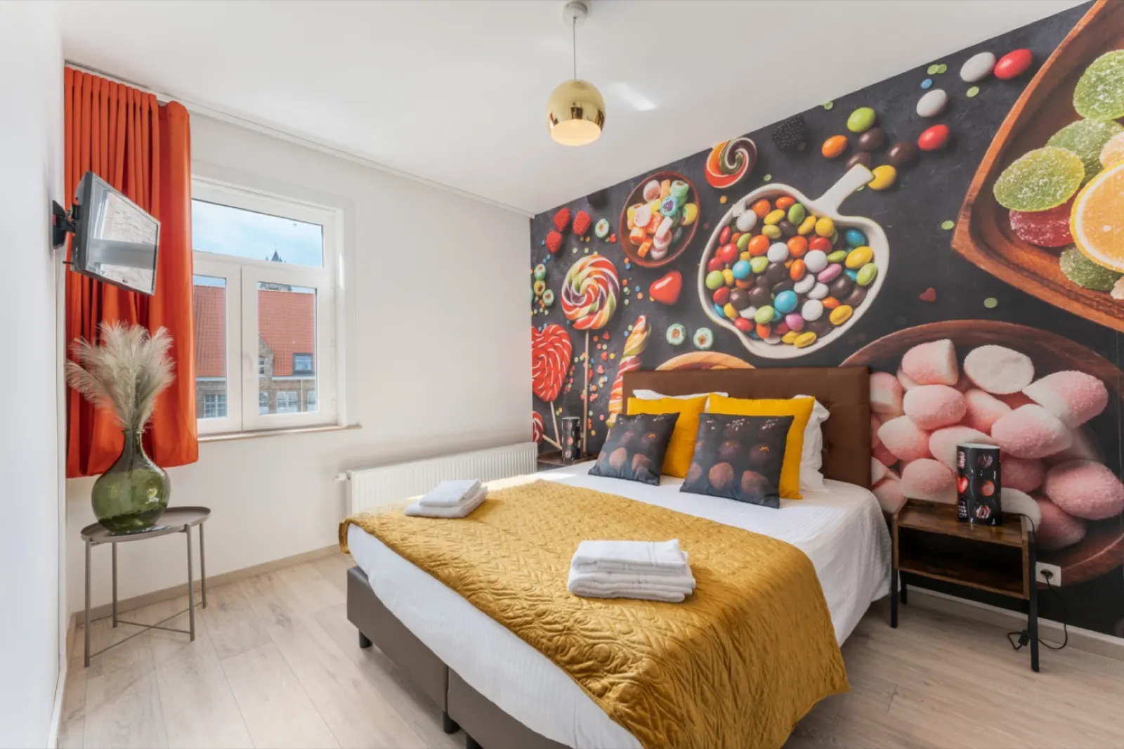 A double bed in front of a wall-size candy mural, with orange curtains