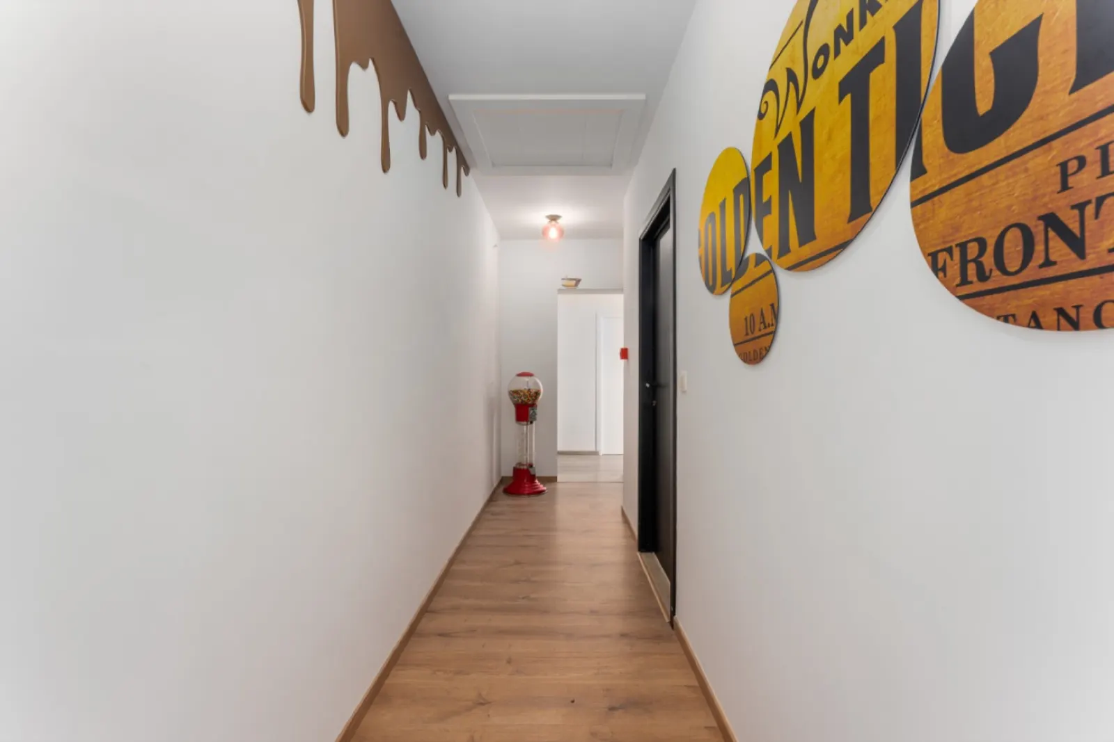 The Golden Ticket hallway in the Candy Family Suite, with a chocolate drip on the wall and a red gumball machine at the end