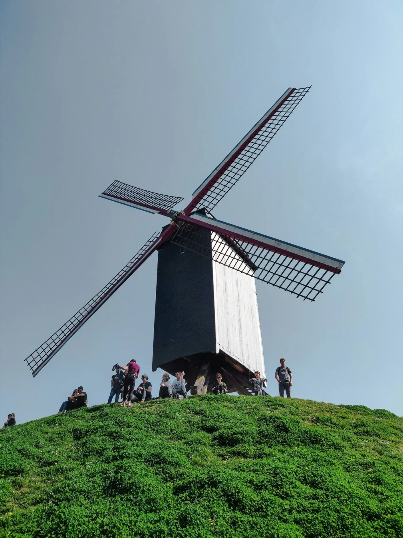 A windmill on its grassy mound on the Bruges ramparts, with people sitting on the slope